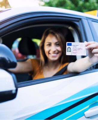Glückliche Fahrschülerin zeigt ihren neuen Führerschein aus dem Autofenster.